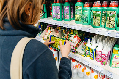 Lady looking at a range of products on a shelf, with a package in her hand of EntoGrow the range includes organic fertiliser and soil conditioner, helping to care for your garden